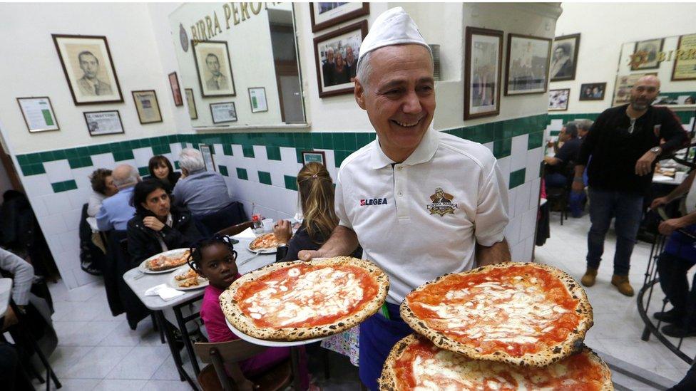 A waiter serves a pizza at L'Antica Pizzeria da Michele in Naples, December 2017