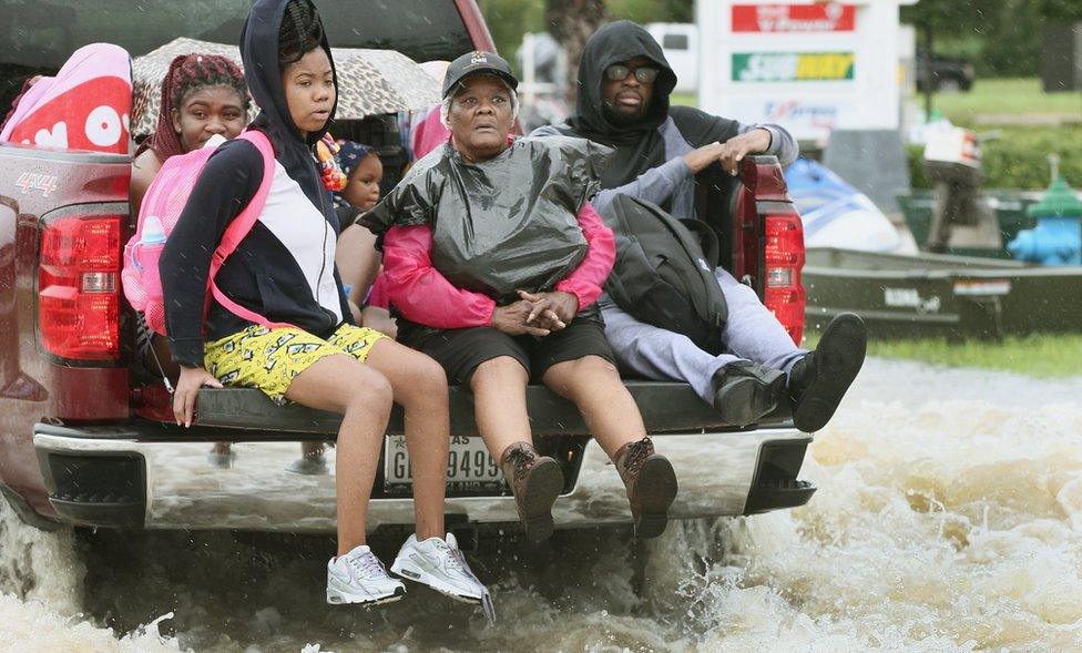 At least five people in the back of a pick up truck as it drives through water