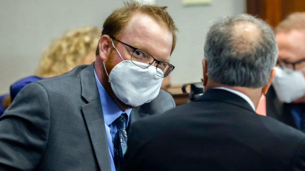 Travis McMichael, masked on the left left, speaks with his attorney