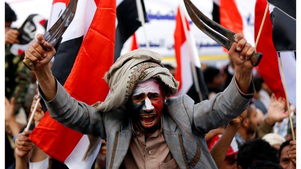 A man waves traditional daggers, or Jambiyas, as he protests against the war in Yemen