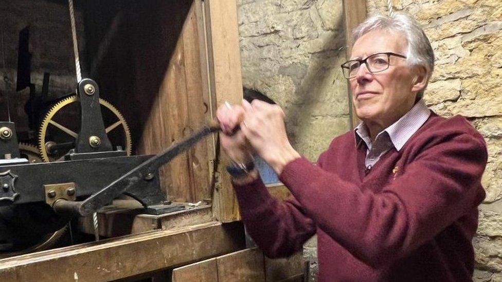 Man wearing red sweater pulls on the handle of a clock mechanism inside a stone tower