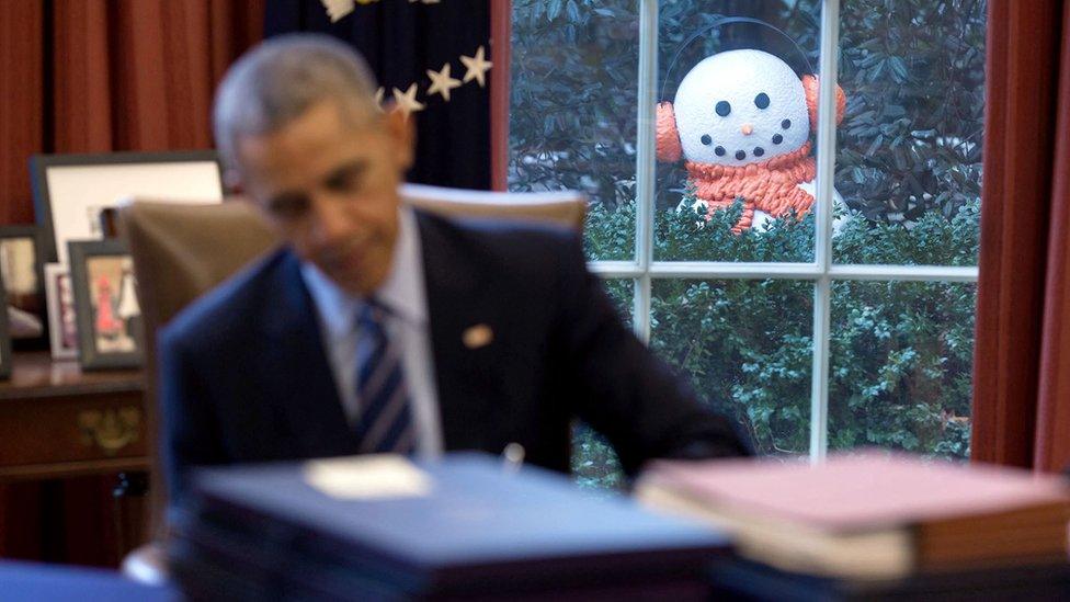 An out-of-focus Mr Obama works at this desk. Visible in the window, in sharp focus, is an elaborate snowman with scarf and earmuffs.