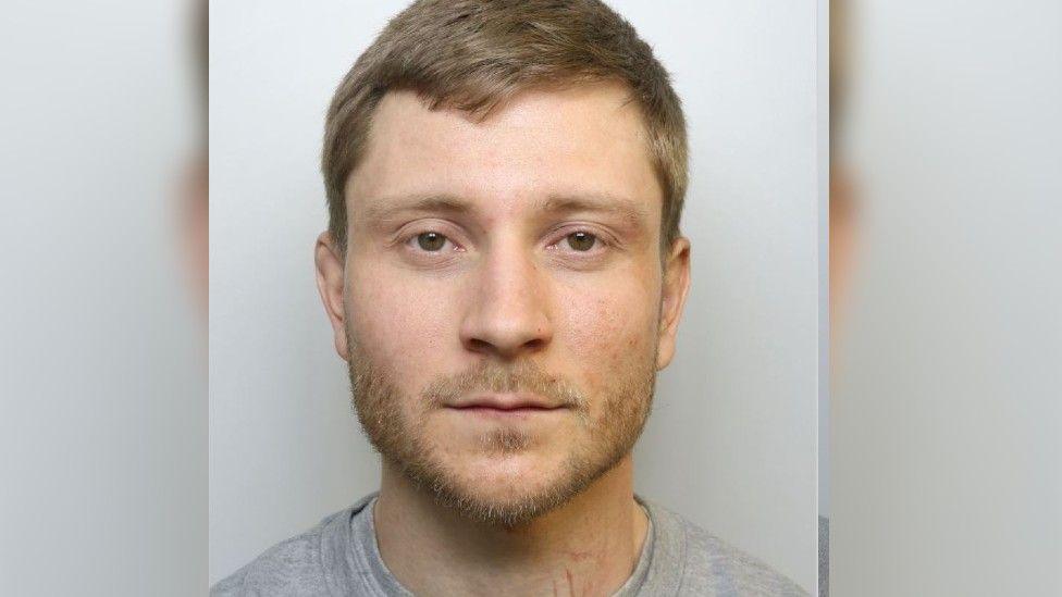 Mugshot of Jones who is wearing a grey top and has brown hair and beard