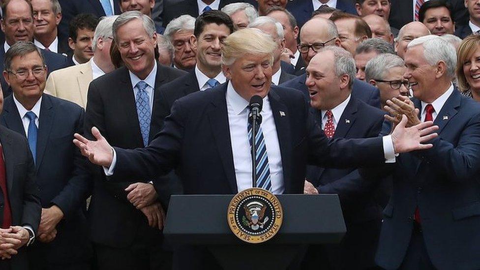 Donald Trump, flanked by aides, speaks about his healthcare act