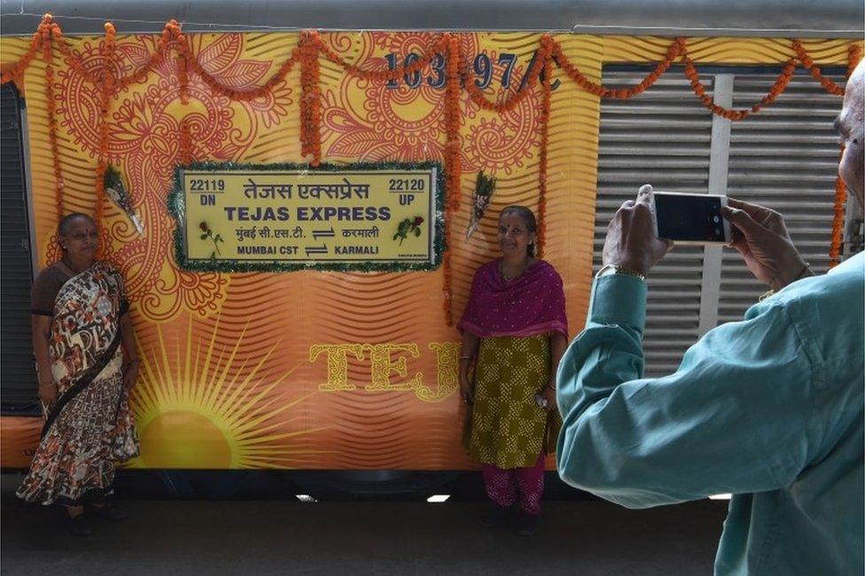 In this photograph taken on May 22, 2017, Indian passengers pose for a photograph alongside the Tejas Express luxury train during its first journey between Mumbai and Goa at Ratnagiri