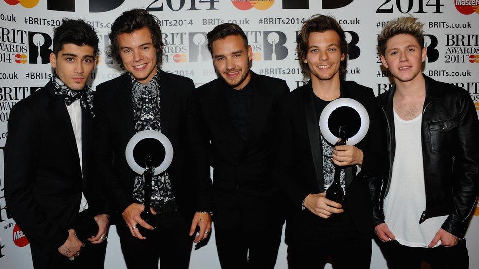 The five members of 1D stand holding two awards at the Brit Awards,