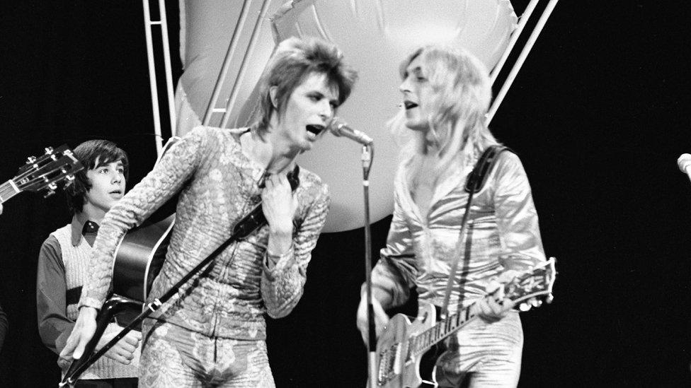 David Bowie singing alongside Mick Ronson who is strumming a guitar