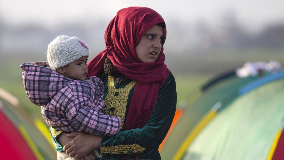 A woman stands outside her tent holding a child in the early morning on the Greek-Macedonia border.