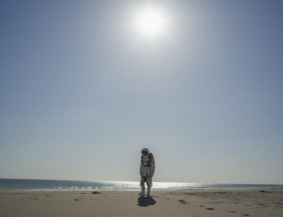 A photo by Cao Fei showing an astronaut walking on an empty beach