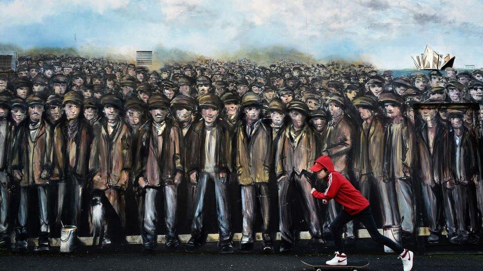 A boy skateboarding past a mural of working class men in Belfast