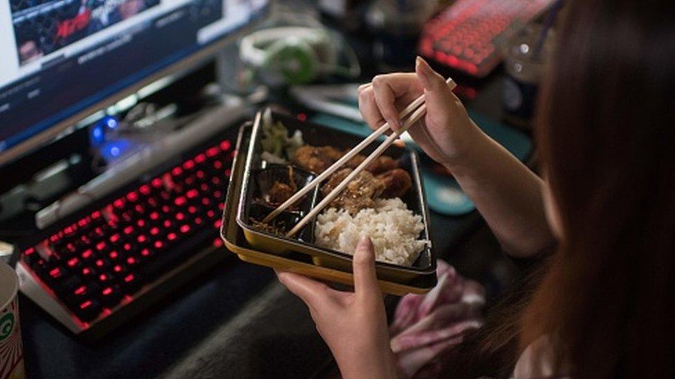 A woman eating alone in front of a laptop