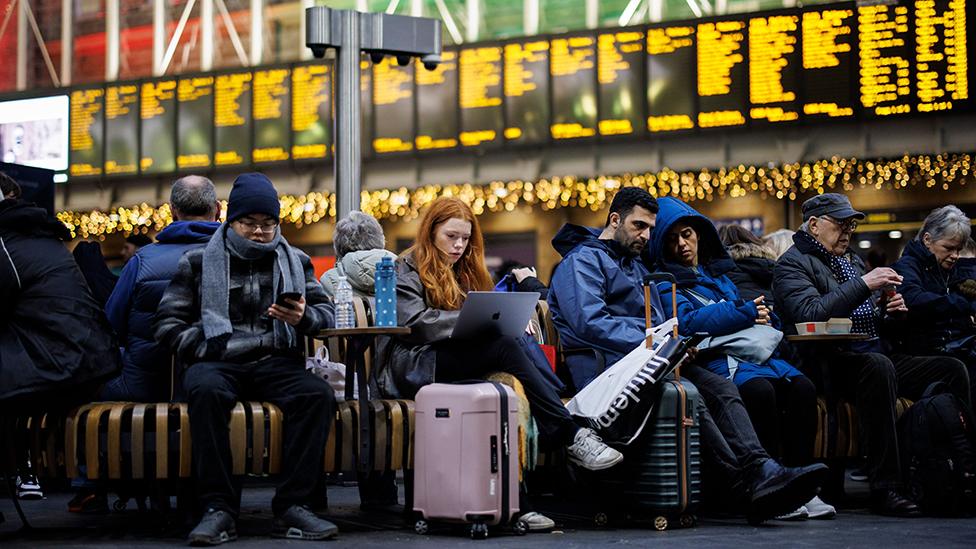 Passengers wait with luggage in front of train departure boards at King's Cross station in London on 27 December