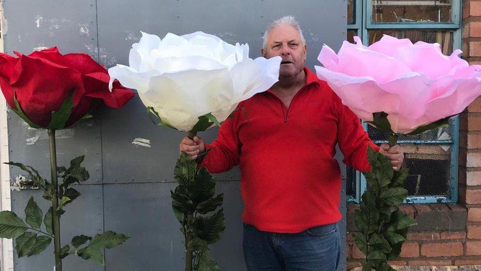 Bill Watson poses alongside large artificial flowers