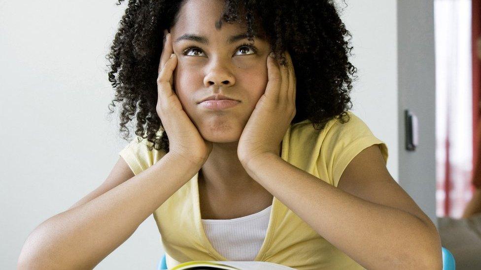 A girl with an afro seated a desk with a book