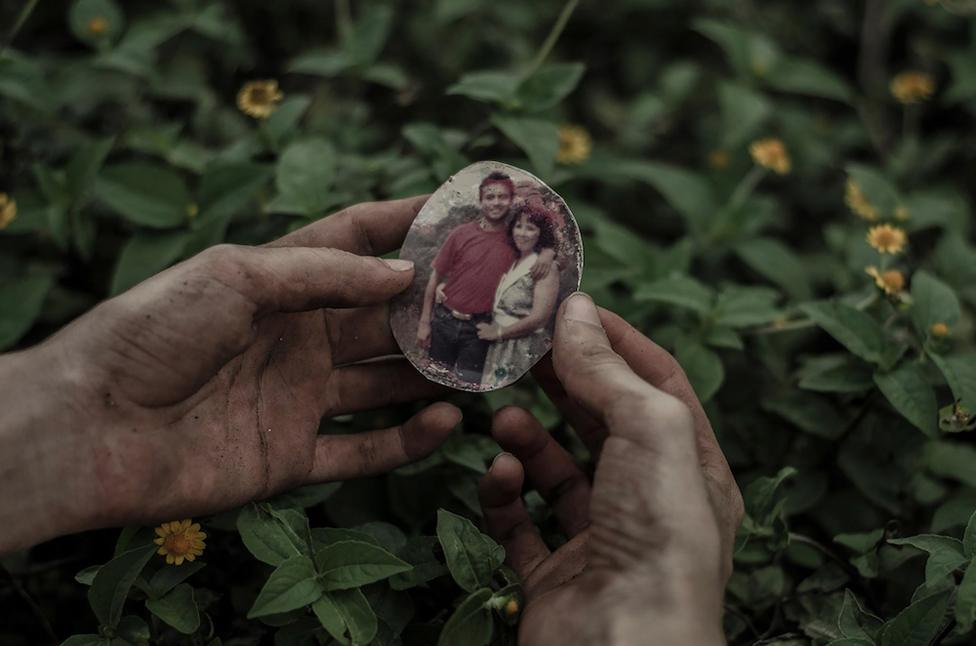 A hand holding a photograph of two people on a locket