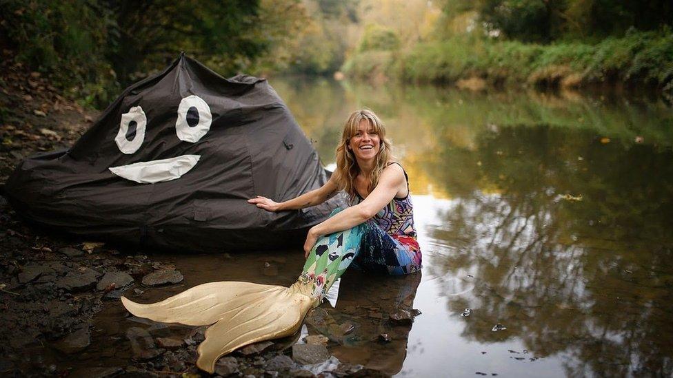 Lindsey Cole wearing a mermaid's tail sitting by a river