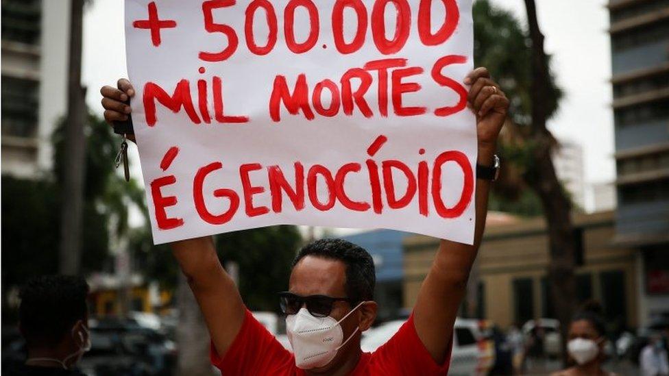 A man at a protest holds a sign calling the deaths genocide