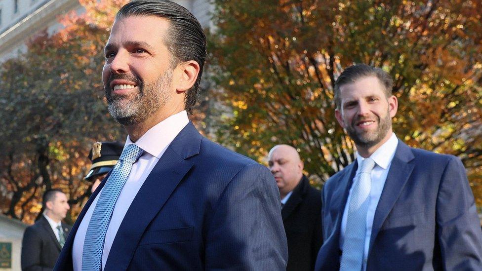 Donald Trump Jr in blue suit with pink shirt and blue tie in front of Eric Trump in blue suit with white shirt and blue tie