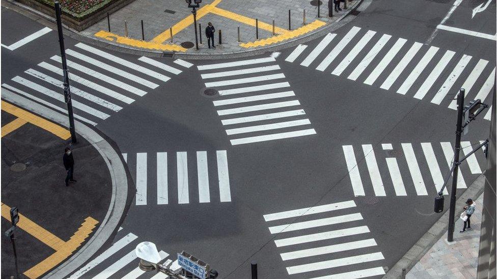 People wait to walk over a pedestrian crossing in Shinjuku during a nationwide a state of emergency in which many shops, restaurants, cafes and businesses have closed, on April 28, 2020 in Tokyo, Japan.