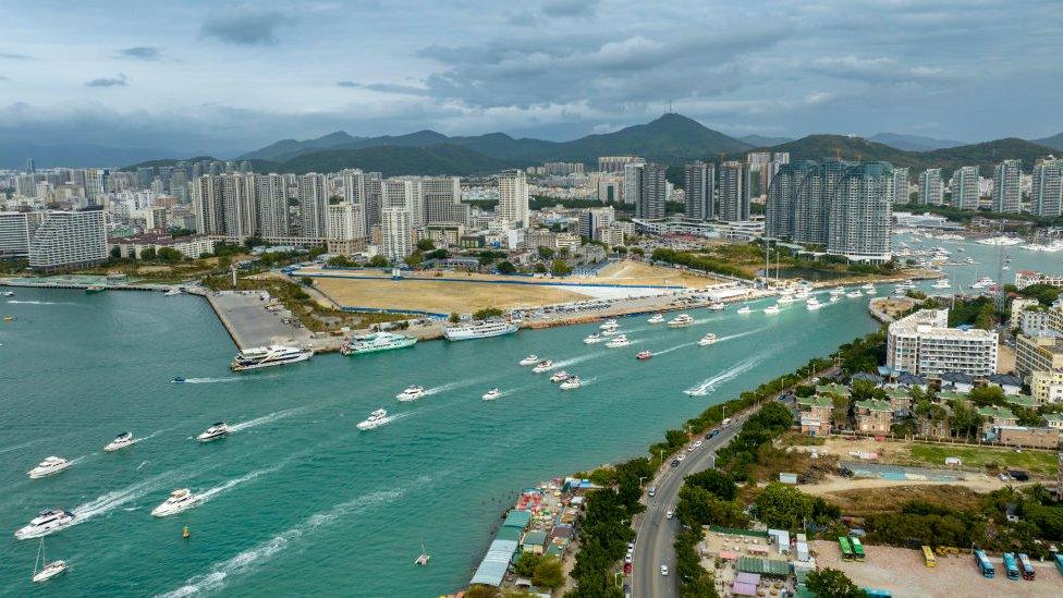 Dozens of boats leave a harbour surrounded by high-rise buildings