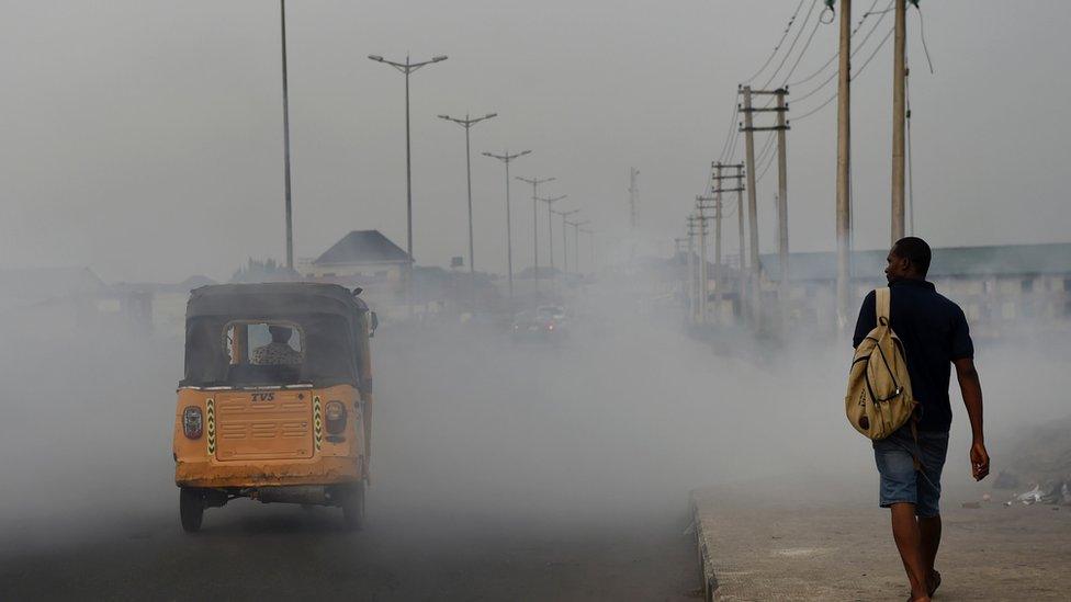 A rickshaw carries passengers through smoke emitted from a dump in the city of Port Harcourt