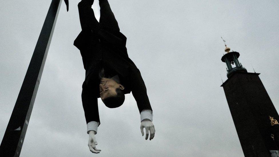 A puppet hanging upside down with Stockholm City Hall visible in the background