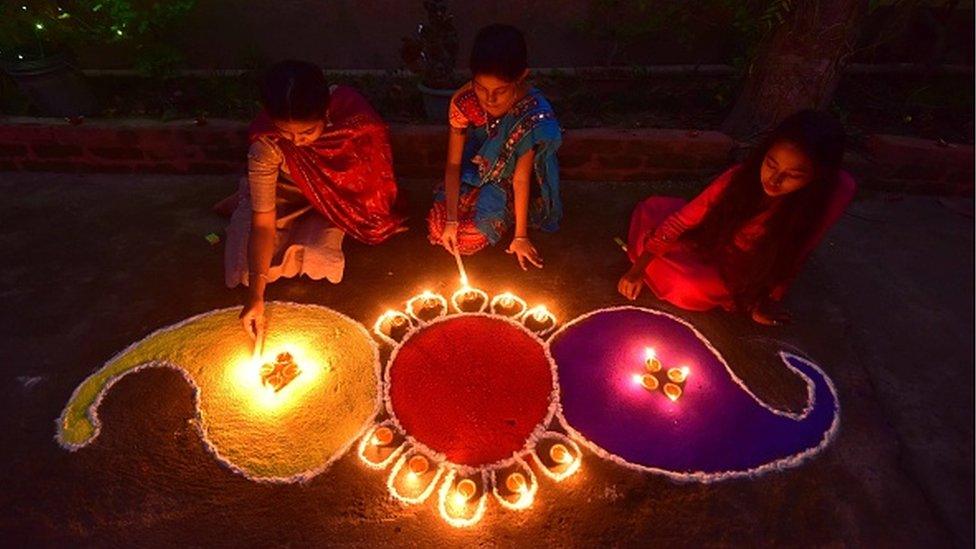 Girls pose after lighting oil lamps around a "Rangoli" in the Nagaon District of Assam