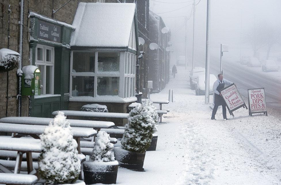 A local butcher carries his shop sign across a snowy pavement in Tow Law, County Durham, as Storm Eunice sweeps across the UK on 18 February 2022