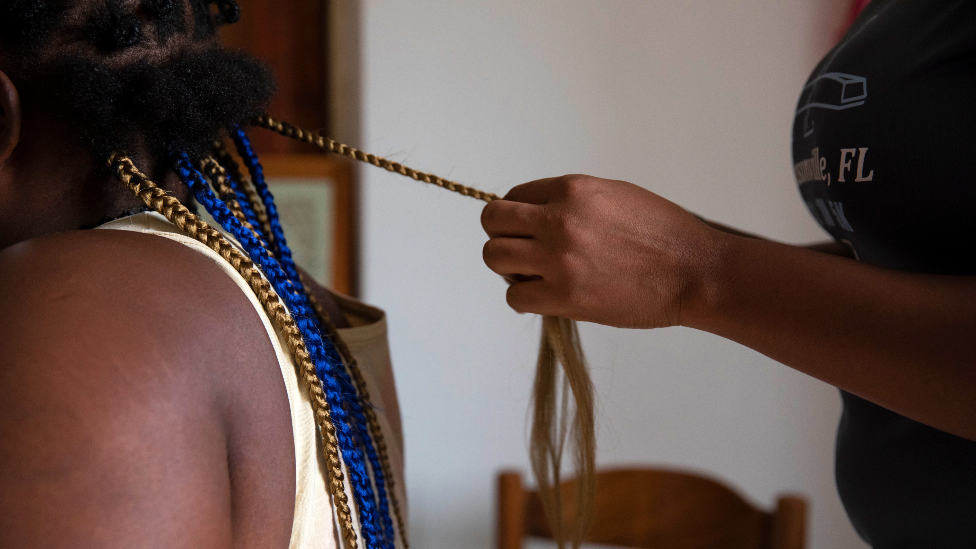 Nigerian woman braids another's hair at a shelter in Sicily after escaping from trafficking networks