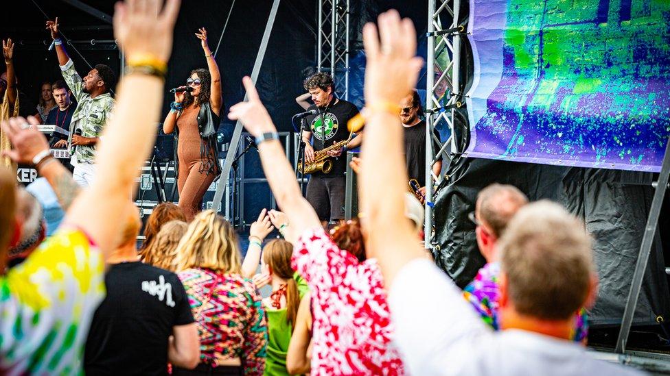 People raising there hands whilst watching a band play on an outdoor stage