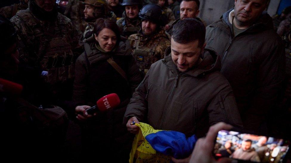 Volodymyr Zelensky holds a national flag as he visits a position of Ukrainian service members in the frontline town of Bakhmut