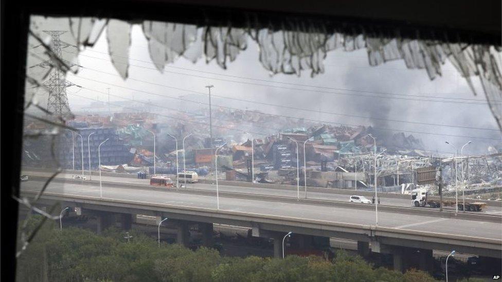 A window shattered by the shockwaves frames the site of an explosion at a warehouse in northeastern China"s Tianjin municipality, Friday, Aug. 14