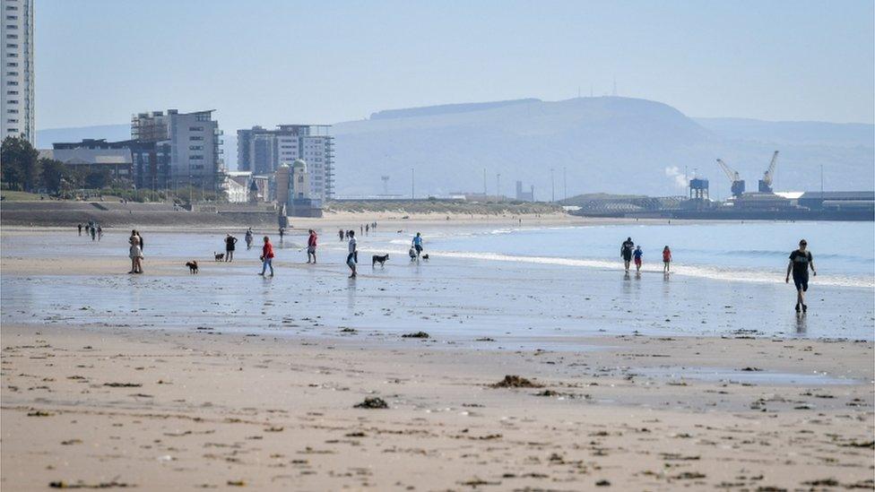 People walk along the beach in hot weather in Swansea, Wales