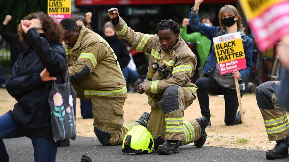 A firefighter in uniform kneels during the protest