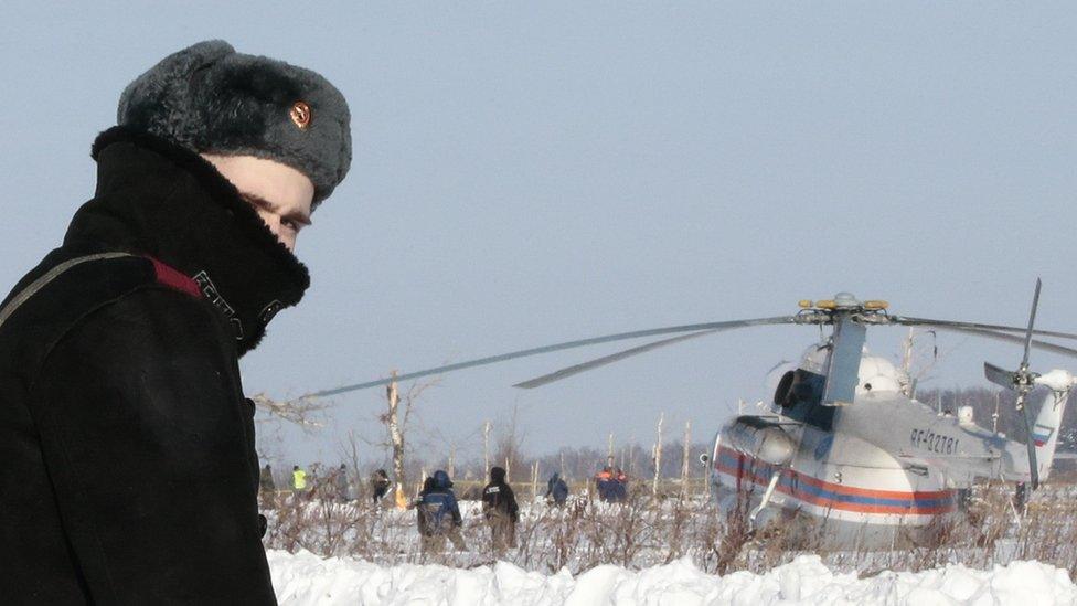 Russian serviceman looking at camera, with helicopter behind him in the snow