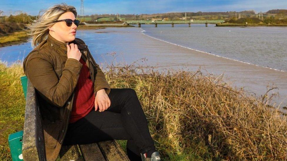 Laura Mathias in a wig on a bench in manningtree