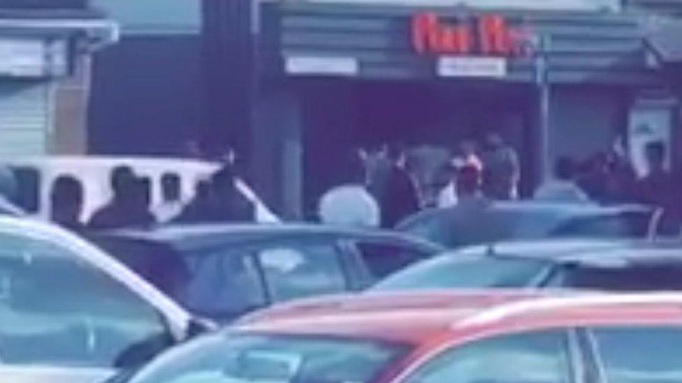 Large group of people gathered outside of a takeaway shop.