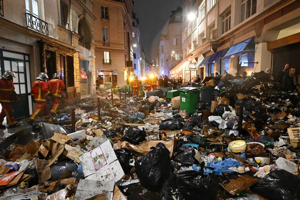 Firefighters checks rubbish after extinguishing a fire during a demonstration, a week after the government pushed a pensions reform through parliament without a vote, using the article 49.3 of the constitution, in Paris on March 23, 2023. - Some 1.089 million protesters took part in demonstrations in France on March 23, 2023, against President Emmanuel Macron's pension reform, the interior ministry said, with 119,000 marching in Paris alone