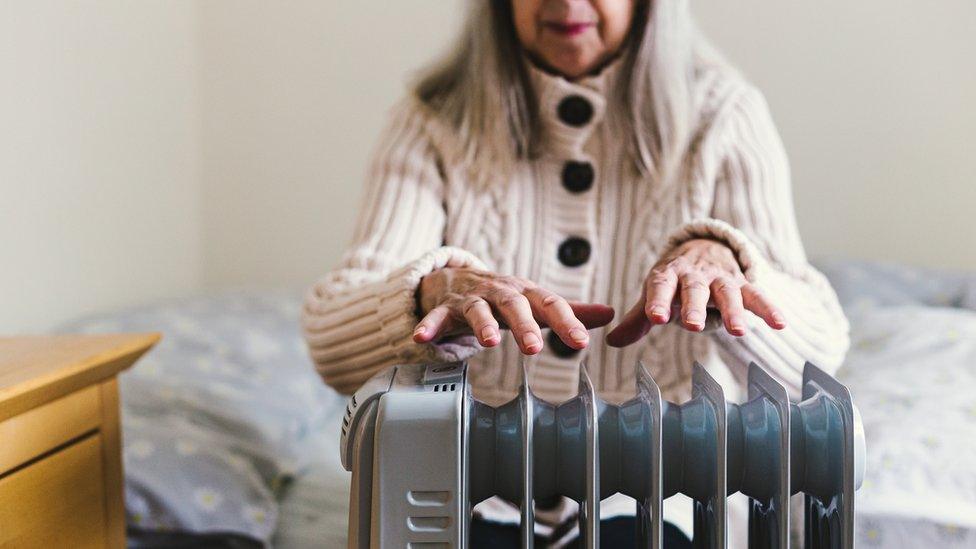 A retired senior woman in her 70s sits at home inside her cold house in winter.