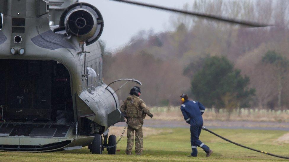 A man with ear defenders on pulls a fuel pipe towards a Chinook