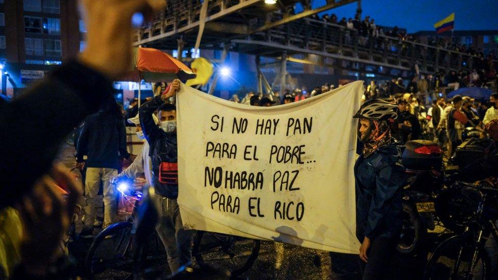 Protesters hold up a sign reading "When there's no bread for the poor, there's no peace for the rich"