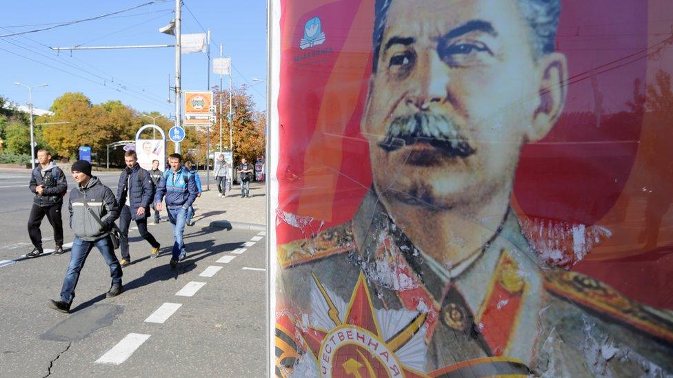 People in Donetsk walk past a poster of Joseph Stalin (18 Oct)