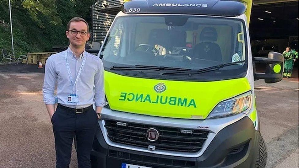 Man with short brown hair wearing a lanyard in front of an ambulance