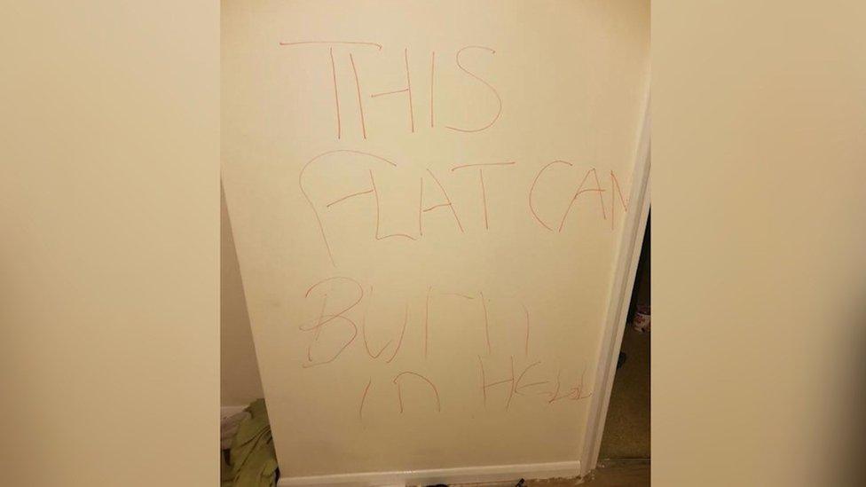 "This flat can burn in hell" written in red capital letters on a wall