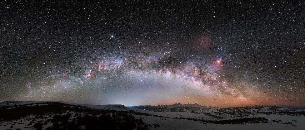 The milky way in full, curving over snowy mountain-tops.