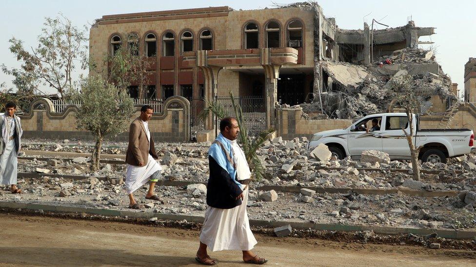 Yemenis walk past a building, housing branches of the Finance Ministry and Central Bank, that was heavily damaged in an airstrike by the Saudi-led coalition, in the northern province of Saada