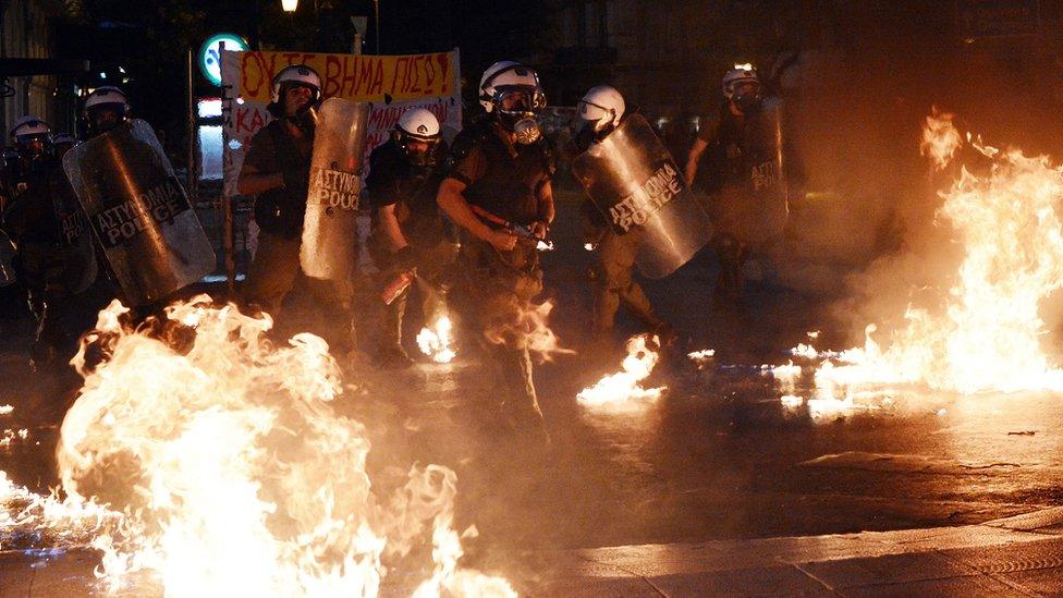 Riot police stand amid petrol bombs threw by protesters during an anti-austerity protest on July 15, 2015.