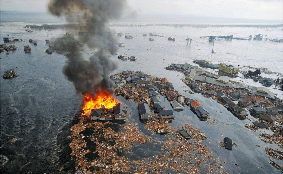 A town swamped with water from the tsunami, with a home burning in the foreground