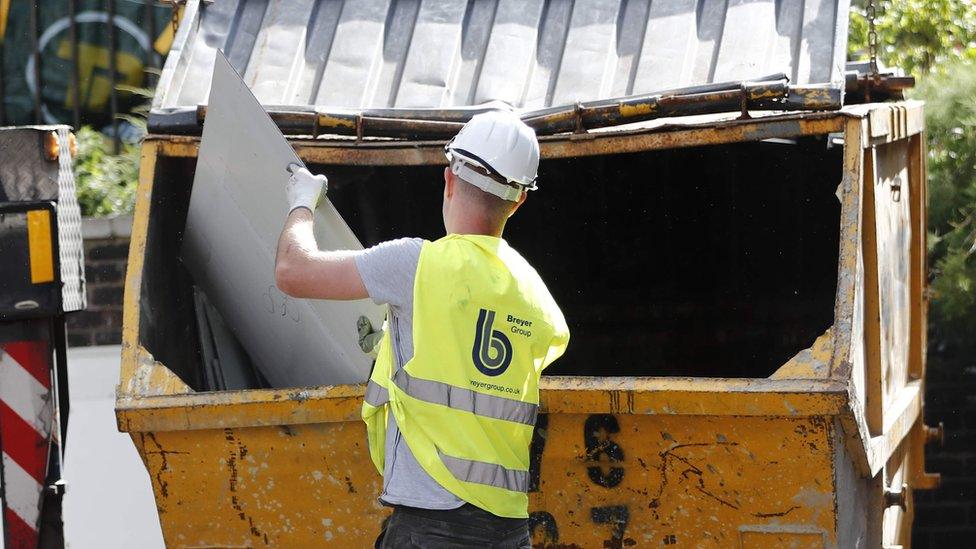 A workman throws a piece of cladding in a skip