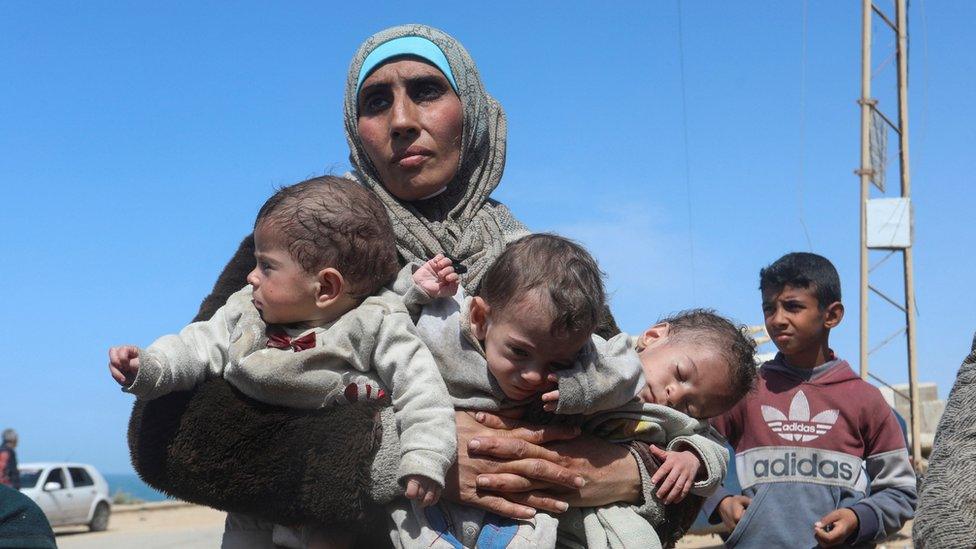 A Palestinian woman fleeing Al Shifa hospital following an Israeli raid, carries her triplet children as she moves southward, amid the ongoing conflict between Israel and Hamas, in the central Gaza Strip March 21, 2024.